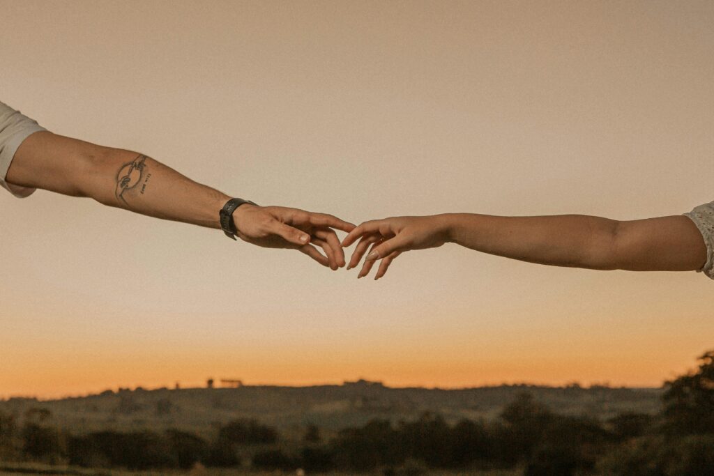 A couple's hands reaching across the sunset sky in Presidente Prudente, Brazil, symbolizing connection.